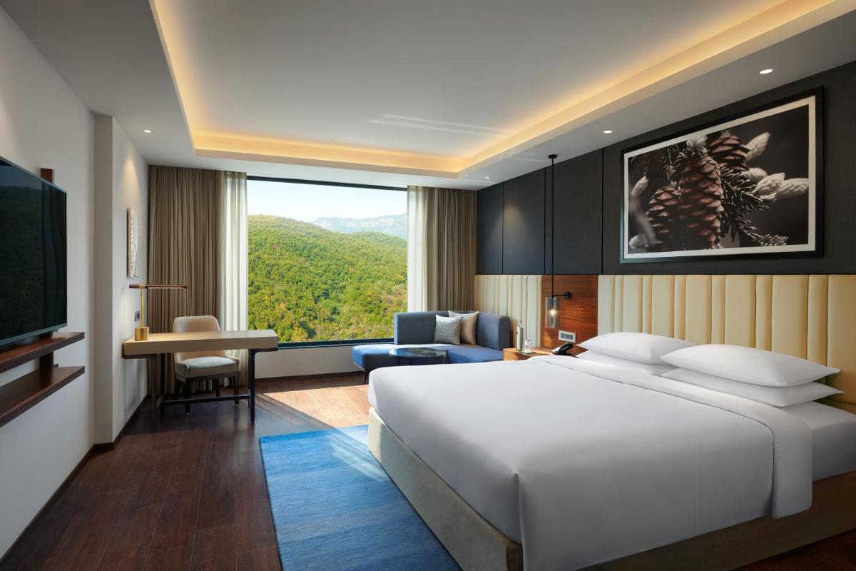 a bedroom with a large white bed and a living room at Hyatt Regency Dehradun Resort and Spa in Dehradun