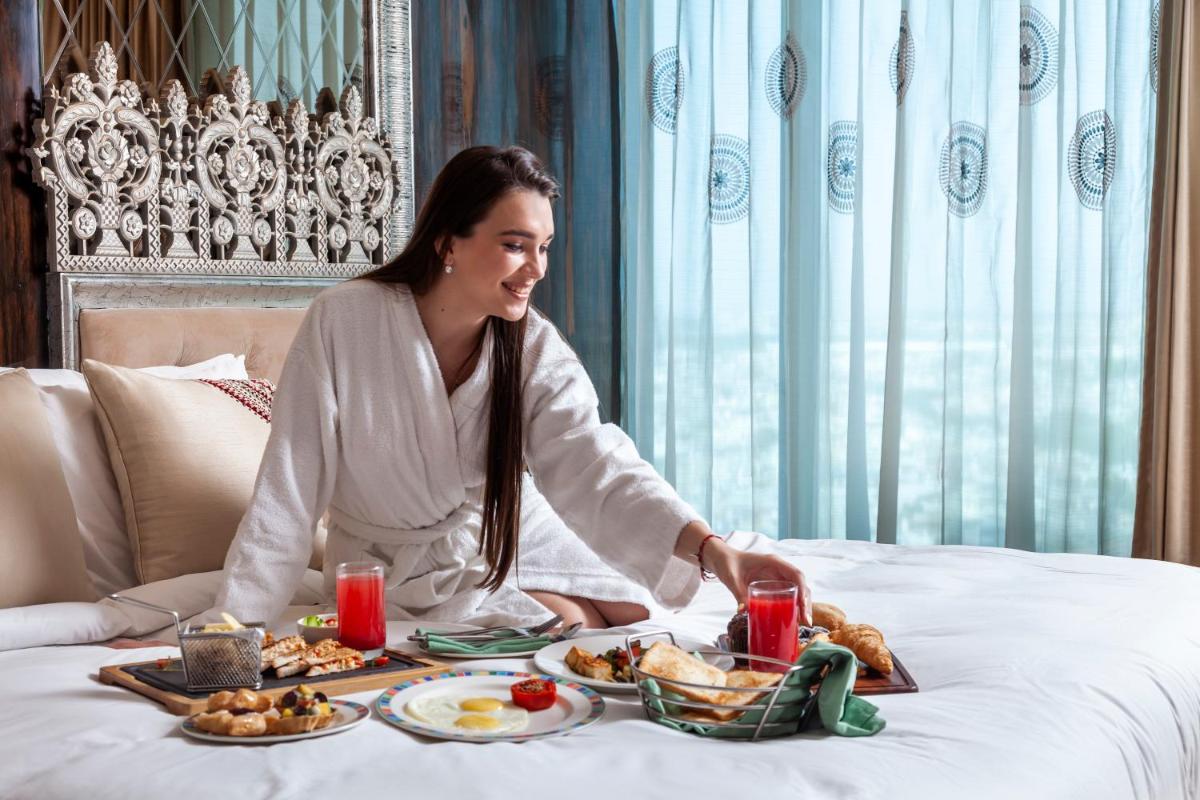 a woman sitting on a bed with a tray of food at Seven Seas Hotel in New Delhi