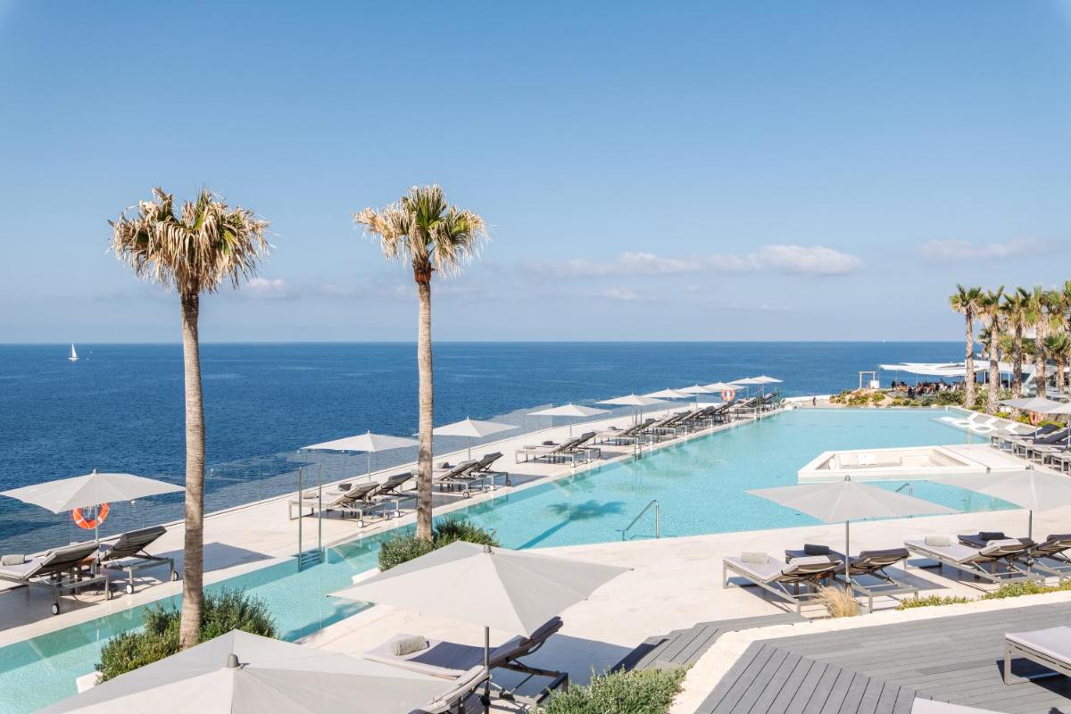 una piscina con sombrillas blancas y el océano en 7Pines Resort Ibiza, part of Destination by Hyatt, en San José