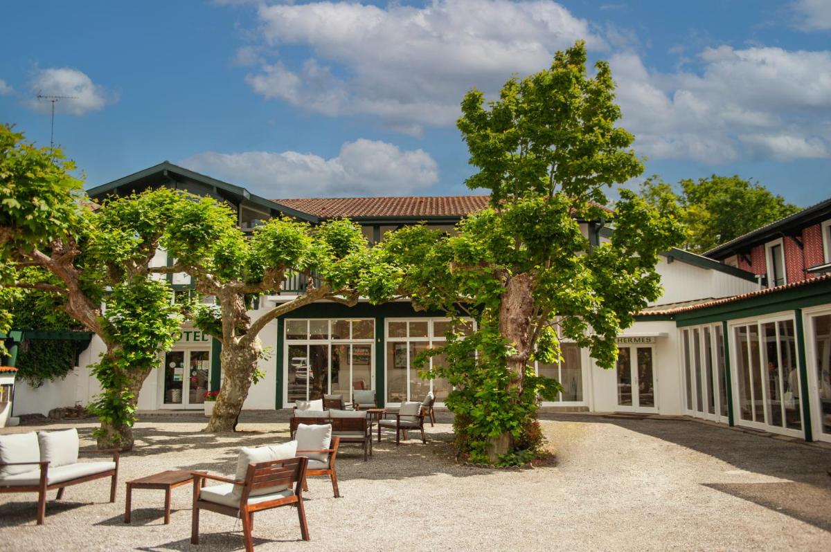 une cour avec des tables et des chaises devant un bâtiment dans l'établissement Logis Thermal, à Saubusse