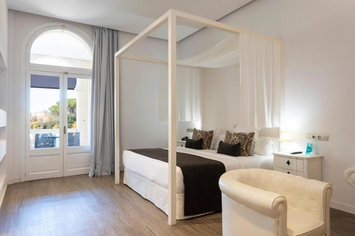 Un dormitorio blanco con una cama con dosel y una silla. en 1881 Hotel Balneario Vichy Catalan, en Caldes de Malavella