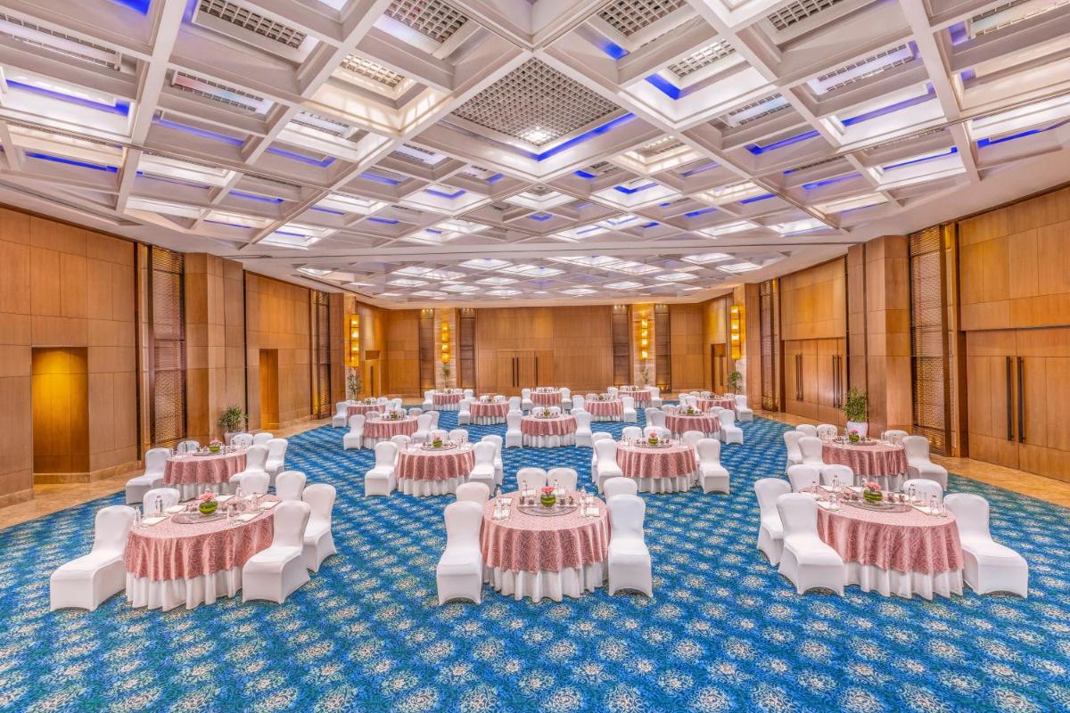 a large banquet hall with tables and white chairs at The Leela Ambience Convention Hotel Delhi in New Delhi