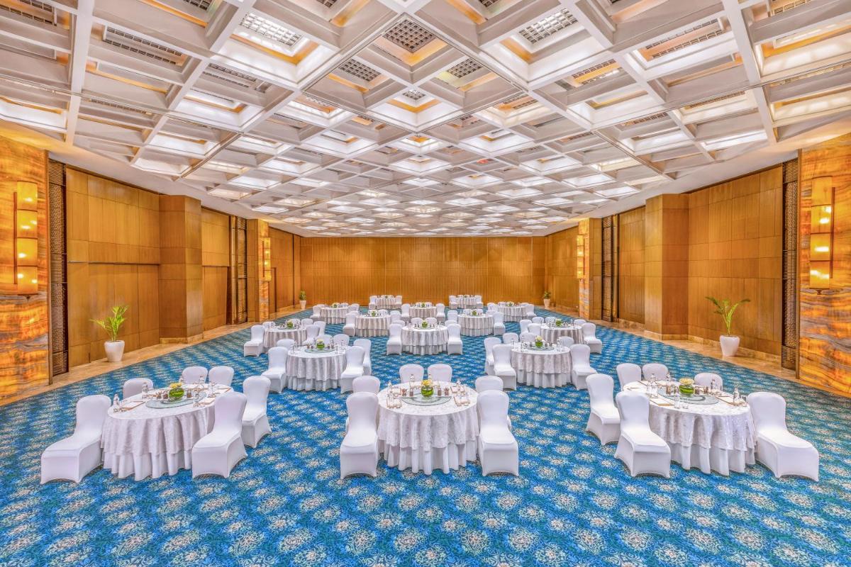 a banquet hall with white tables and white chairs at The Leela Ambience Convention Hotel Delhi in New Delhi