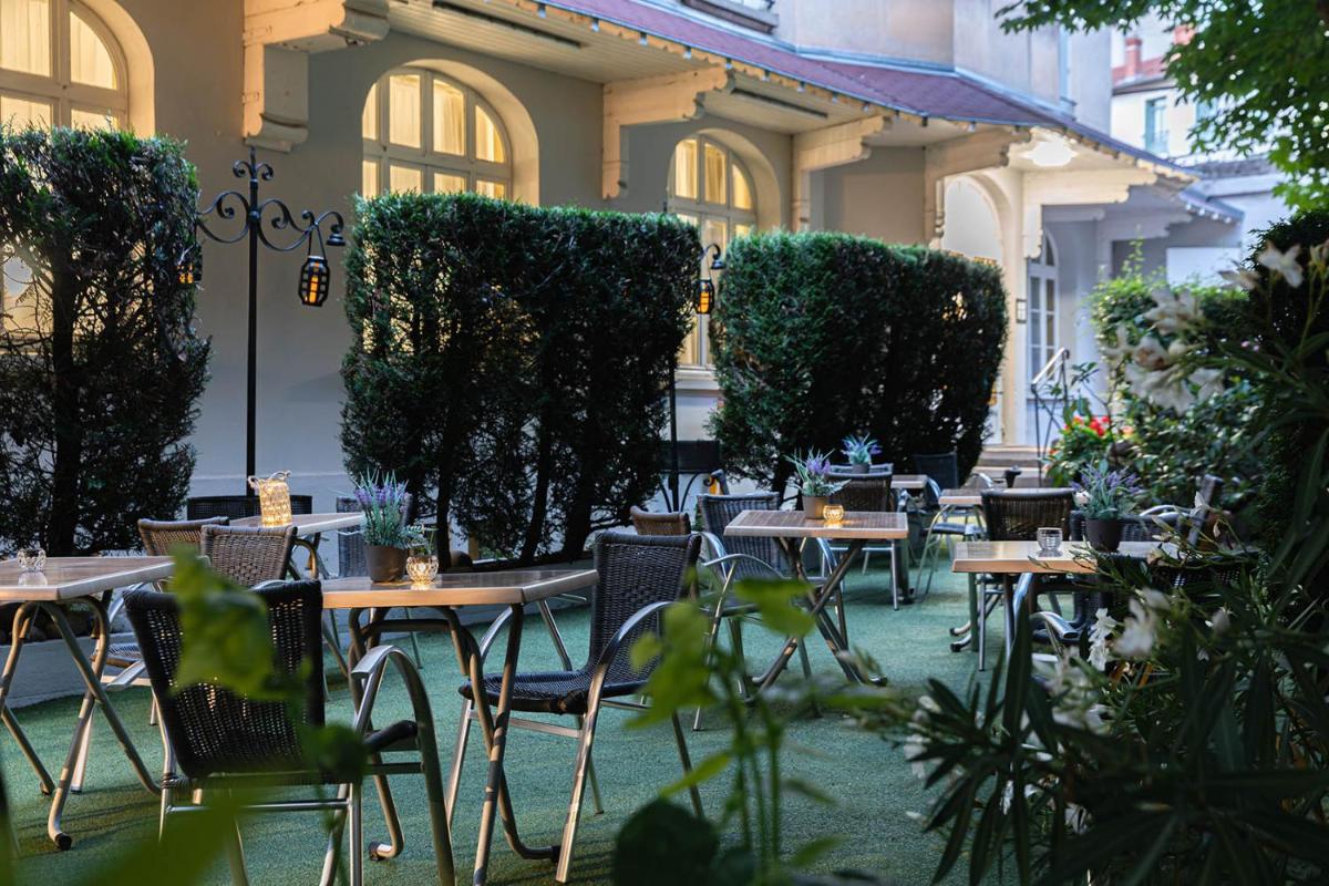 un patio extérieur avec tables, chaises et plantes dans l'établissement The Originals City, Hôtel Bristol, Le Puy-en-Velay, au Puy-en-Velay