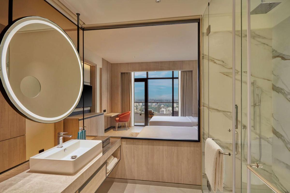 a bathroom with a sink and a mirror and a bedroom at Hilton Gurugram Baani City Centre in Gurgaon