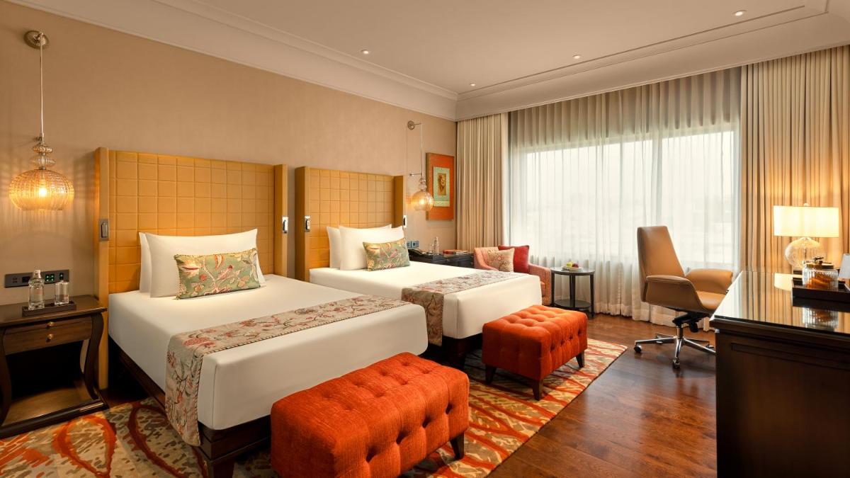 a hotel room with two beds and a chair at The Leela Hyderabad Banjara Hills in Hyderabad