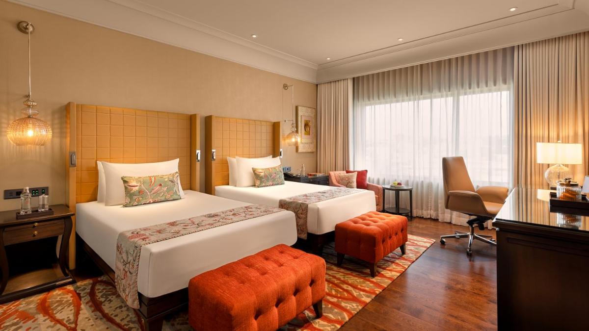 a hotel room with two beds and a chair at The Leela Hyderabad Banjara Hills in Hyderabad