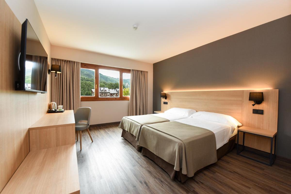 una habitación de hotel con una cama y un televisor en SOMMOS Hotel Benasque Spa, en Benasque