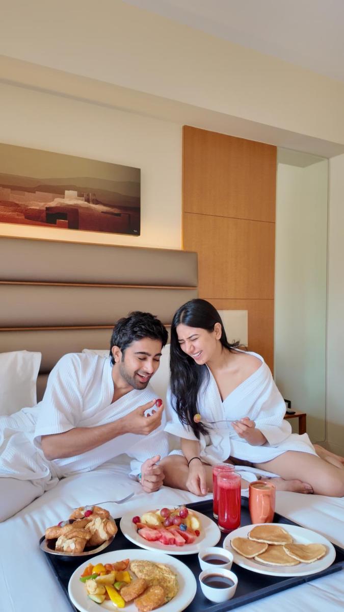 a man and woman sitting on a bed with plates of food at Hyatt Regency Pune Hotel & Residences in Pune