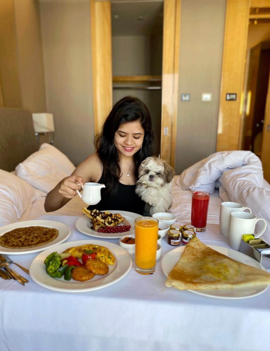 a woman sitting at a table with food and a dog at Hyatt Regency Pune Hotel & Residences in Pune
