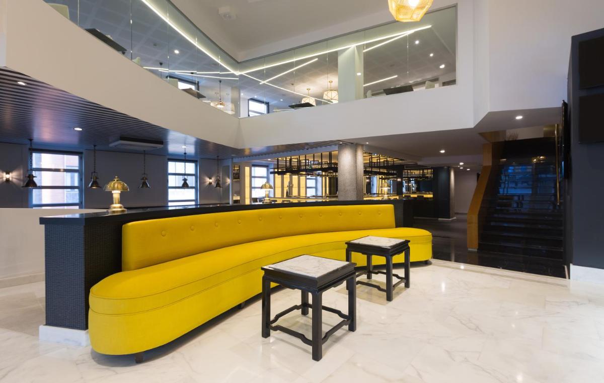 un sofá amarillo en un vestíbulo con dos taburetes en Hotel Mercure Jardines de Albia, en Bilbao