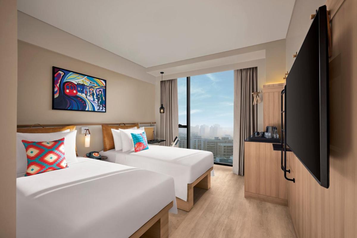 a hotel room with two beds and a large window at Moxy Mumbai Andheri West in Mumbai