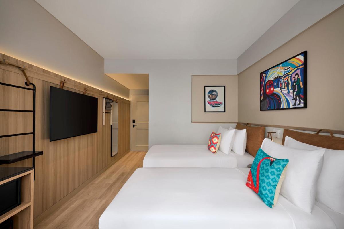 two beds in a hotel room with a flat screen tv at Moxy Mumbai Andheri West in Mumbai