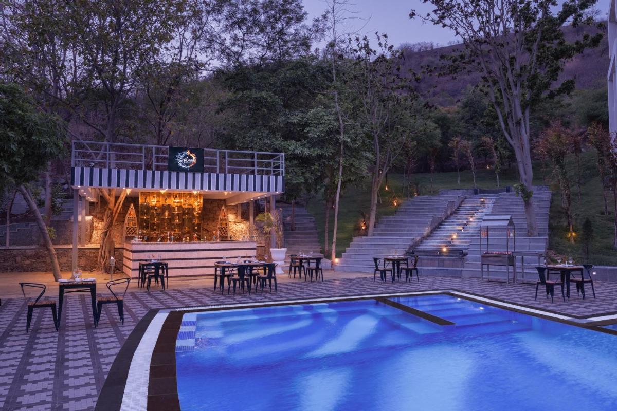 a pool with tables and chairs next to a building at Essentia Luxury Resort & Spa Udaipur in Udaipur