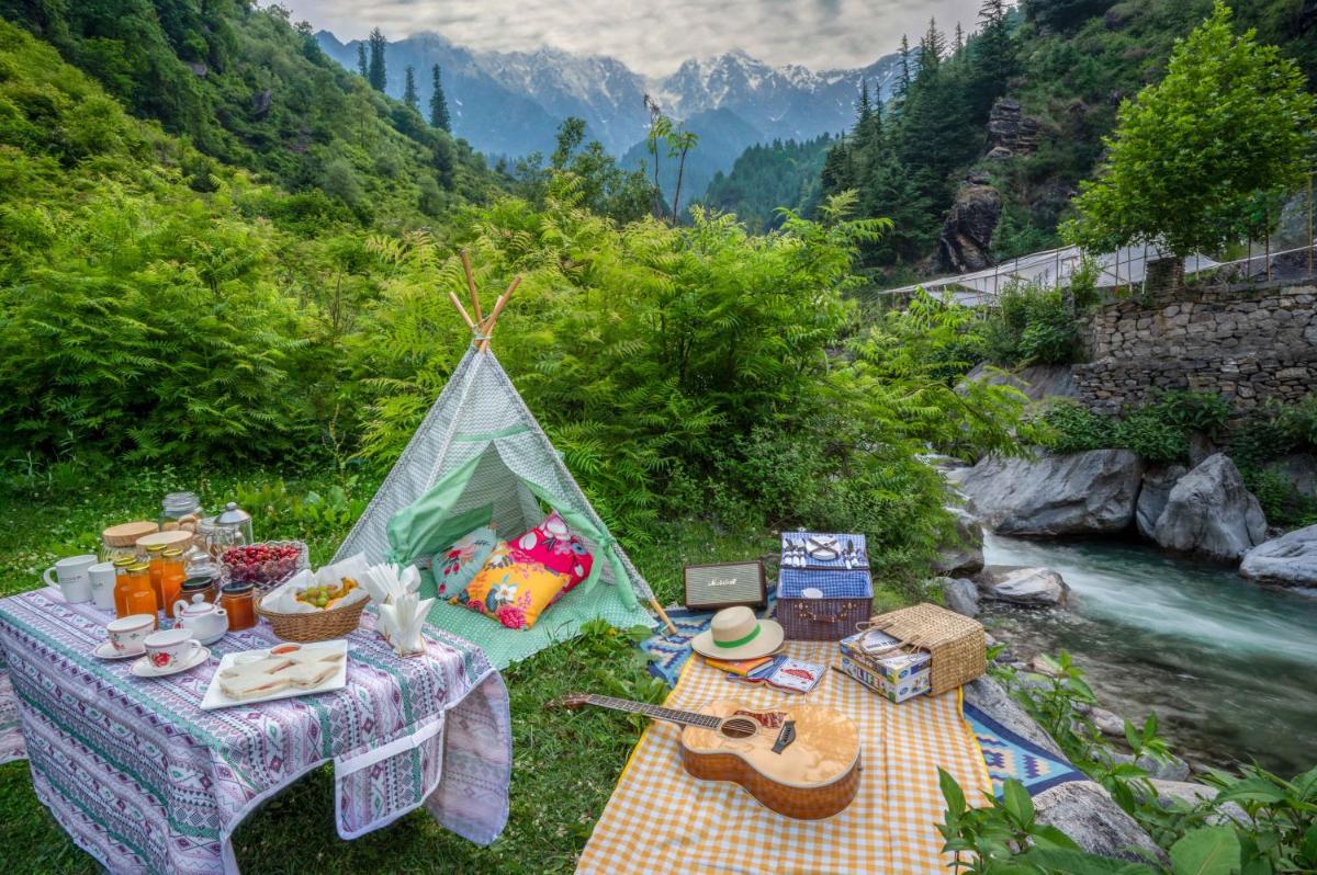 a picnic table with a tent next to a river at Storii By ITC Hotels Urvashis Retreat, Manali in Manāli a picnic table with a tent next to a river at Storii By ITC Hotels Urvashis Retreat, Manali in Manāli