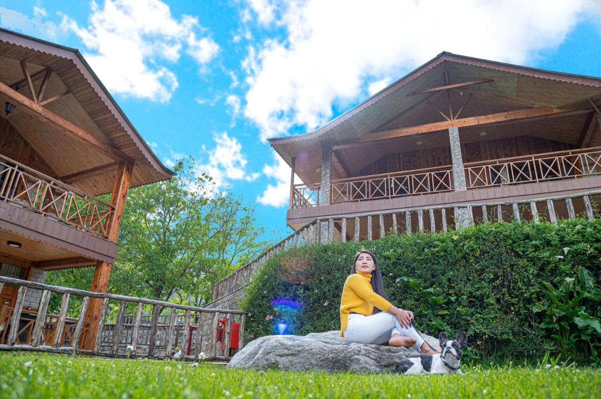 a woman sitting on a rock with a dog in front of a building at Storii By ITC Hotels Urvashis Retreat, Manali in Manāli a woman sitting on a rock with a dog in front of a building at Storii By ITC Hotels Urvashis Retreat, Manali in Manāli