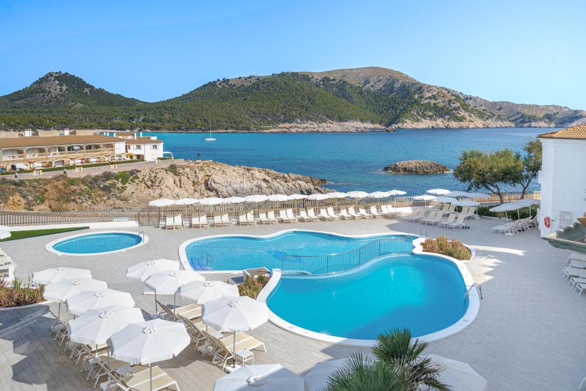 Una piscina con sombrillas y sillas y el océano. en THB Guya Playa, en Cala Ratjada