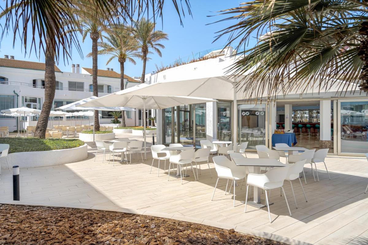Un restaurante con mesas y sillas blancas y palmeras. en THB Guya Playa, en Cala Ratjada