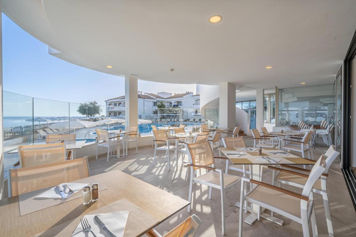 Un restaurante con mesas y sillas y vista al mar. en THB Guya Playa, en Cala Ratjada