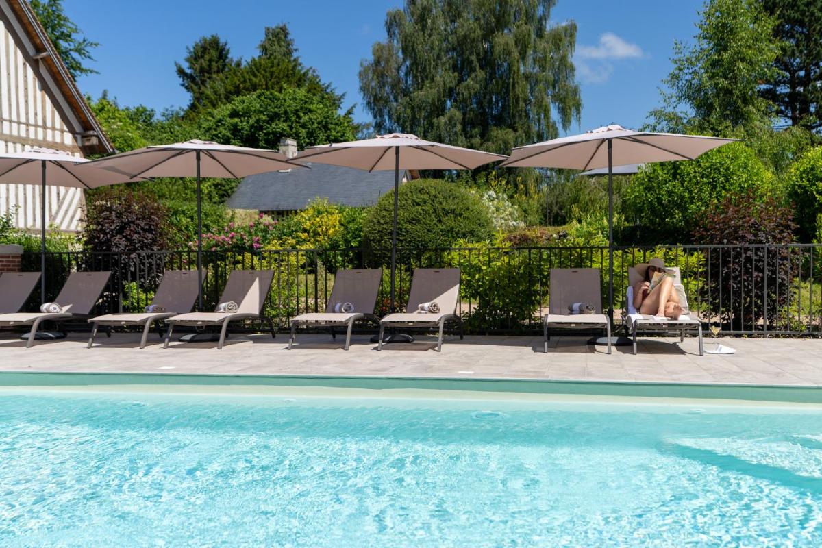 une femme assise dans des chaises à côté d'une piscine avec parasols dans l'établissement Les Manoirs des Portes de Deauville - Small Luxury Hotel Of The World, à Deauville
