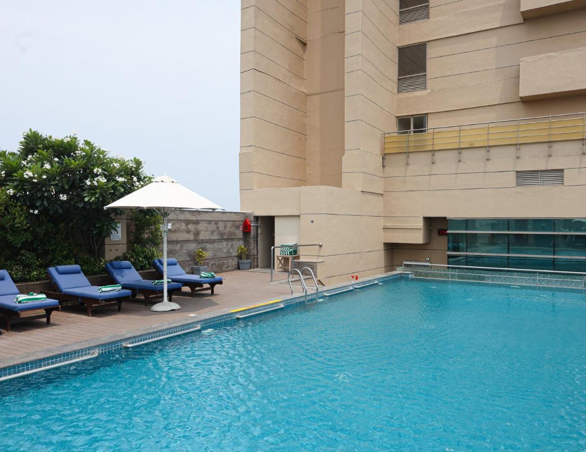 a swimming pool with chairs and an umbrella next to a building at Holiday Inn Chennai OMR IT Expressway by IHG in Chennai