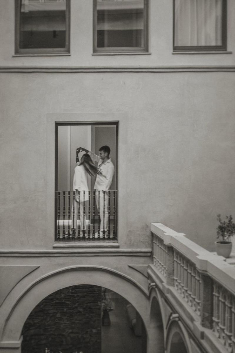 Una pareja de pie en un balcón de un edificio en Hotel Palau Macelli & Spa, en Castelló d'Empúries