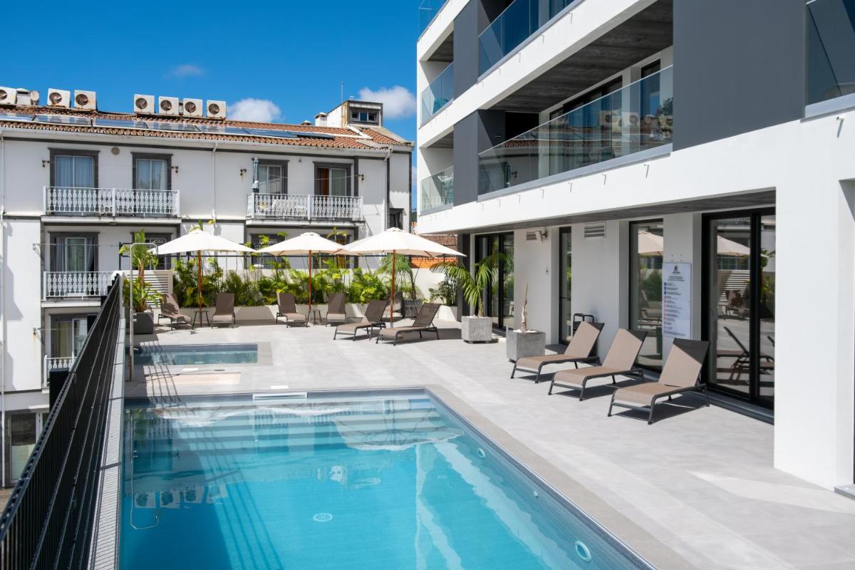 uma piscina exterior com cadeiras e guarda-sóis num edifício em Alto do Forte em Ponta Delgada