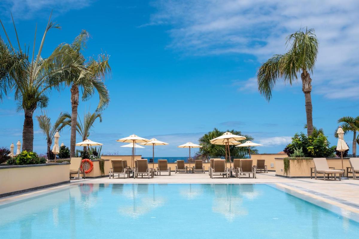una piscina con palmeras, sillas y sombrillas en GF GRAN COSTA ADEJE*****, en Adeje