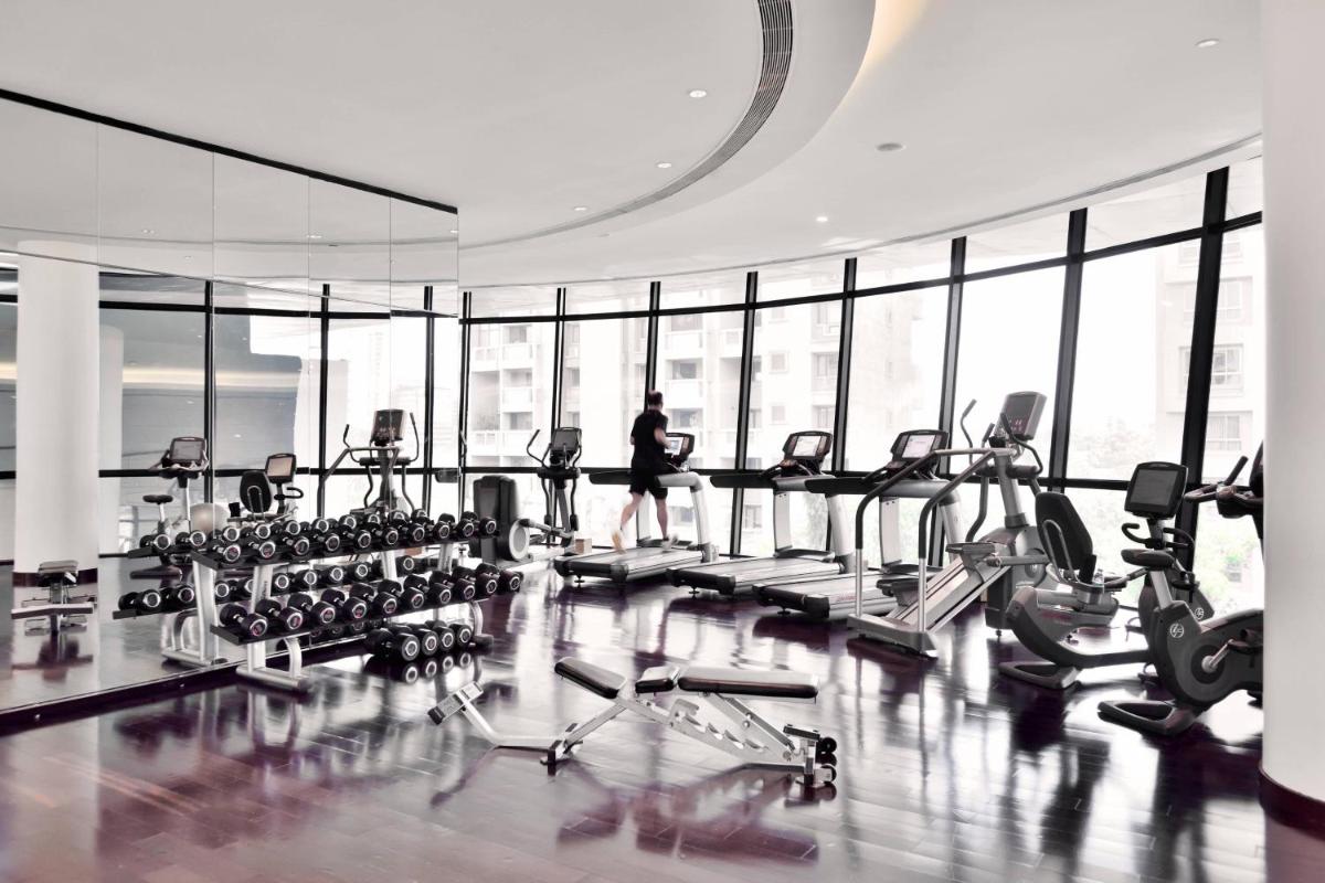 a gym with tread machines and a person in the background at Marriott Suites Pune in Pune