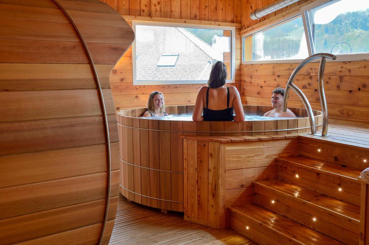 deux personnes dans un jacuzzi dans une pièce en bois dans l'établissement Logis Hôtel Les Autanes & Spa, à Ancelle