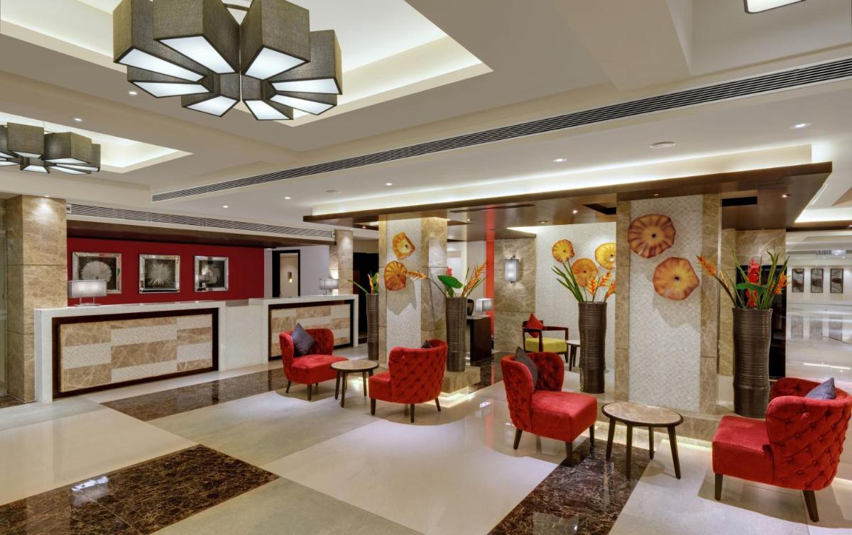 a lobby with red chairs and a fireplace at The Fern Kadamba Hotel And Spa in Old Goa