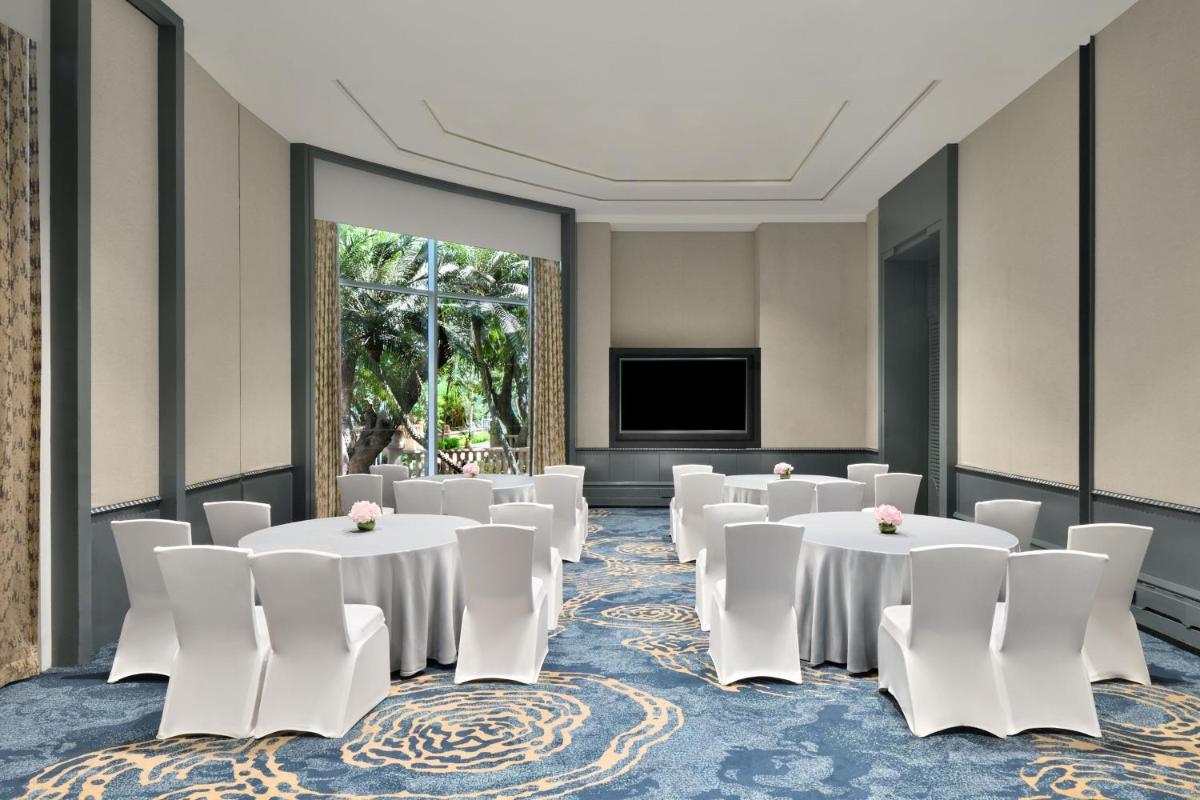 a room with tables and white chairs and a flat screen tv at The Westin Mumbai Powai Lake in Mumbai