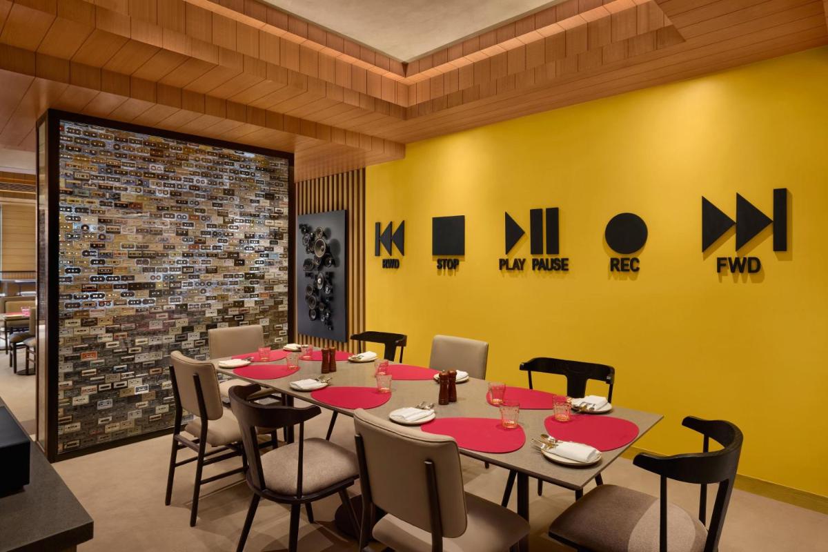 a dining room with a table and chairs and a yellow wall at Moxy Mumbai Andheri West in Mumbai