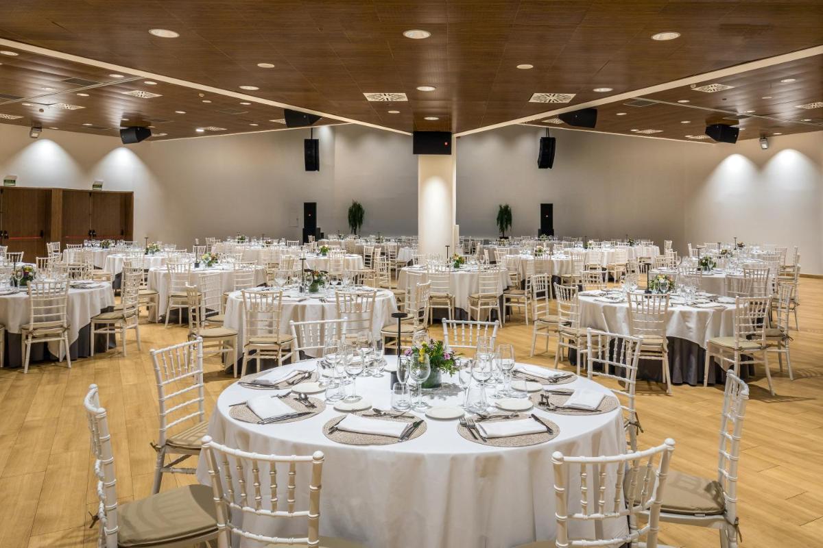 Un salón de banquetes con mesas y sillas blancas. en Barceló Granada Congress, en Granada