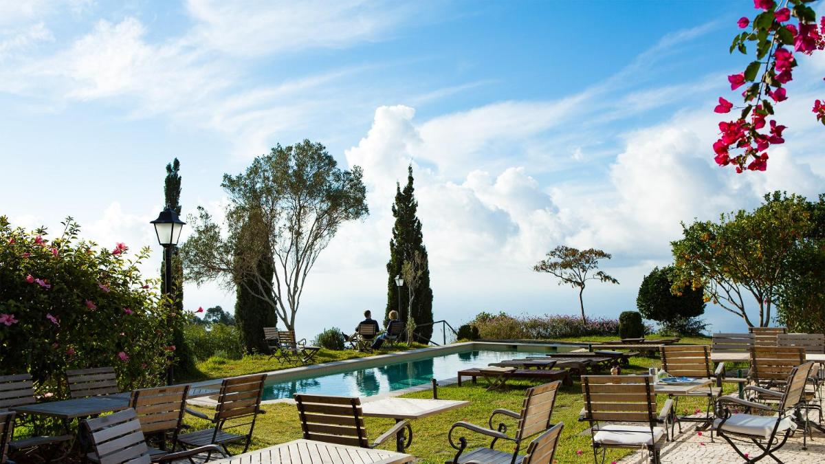 uma piscina com cadeiras e mesas de madeira em Atrio em Estreito da Calheta