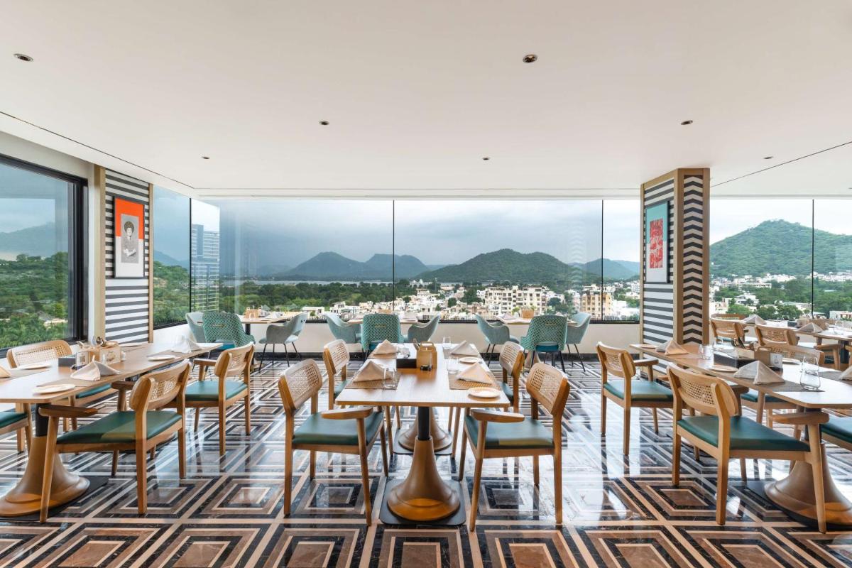 a restaurant with tables and chairs and mountains in the background at Parallel Hotel Udaipur, a member of Radisson Individuals in Udaipur