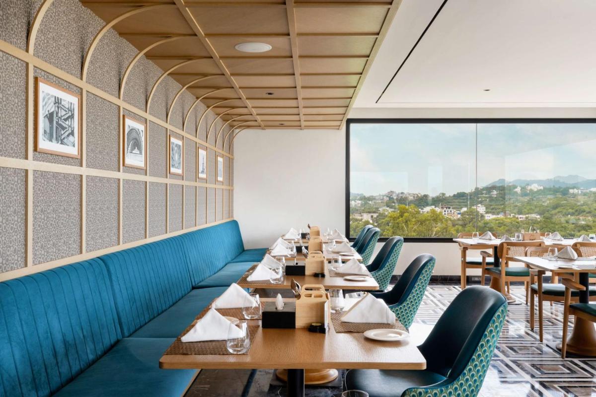 a restaurant with wooden tables and chairs and a large window at Parallel Hotel Udaipur, a member of Radisson Individuals in Udaipur
