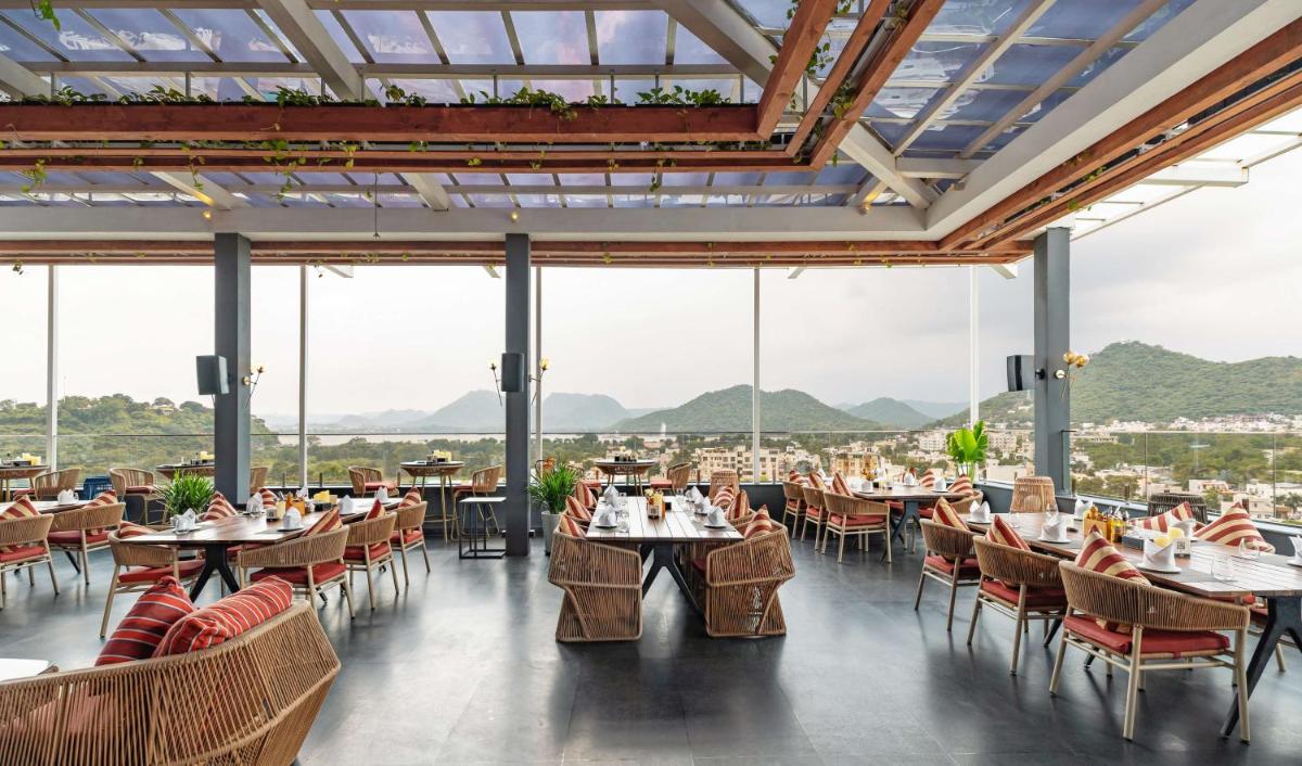 a restaurant with tables and chairs with mountains in the background at Parallel Hotel Udaipur, a member of Radisson Individuals in Udaipur
