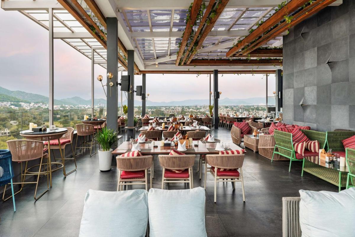 a restaurant with tables and chairs and mountains in the background at Parallel Hotel Udaipur, a member of Radisson Individuals in Udaipur