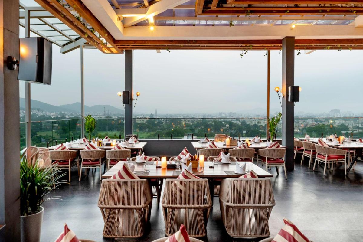 a restaurant with tables and chairs and large windows at Parallel Hotel Udaipur, a member of Radisson Individuals in Udaipur