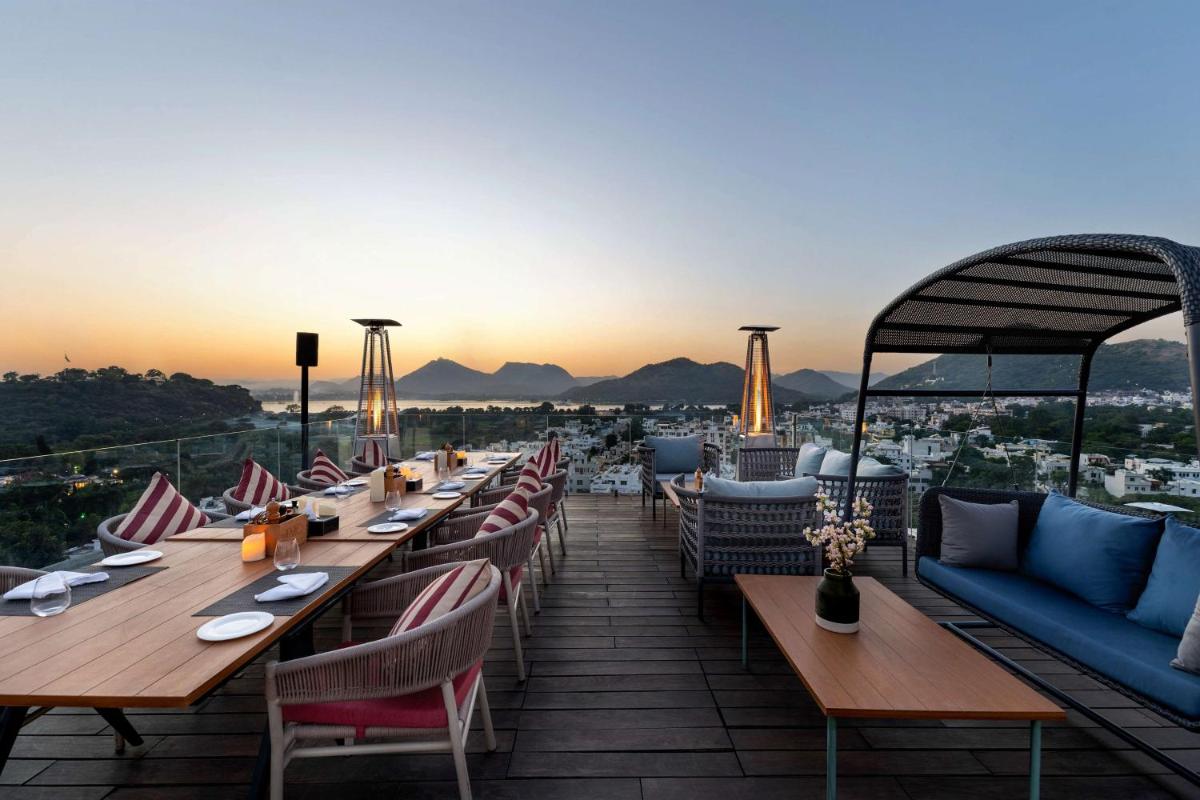 a restaurant with tables and chairs on a roof with the sunset at Parallel Hotel Udaipur, a member of Radisson Individuals in Udaipur