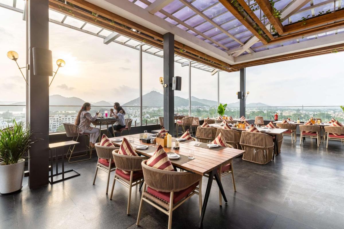 a restaurant with tables and chairs with mountains in the background at Parallel Hotel Udaipur, a member of Radisson Individuals in Udaipur