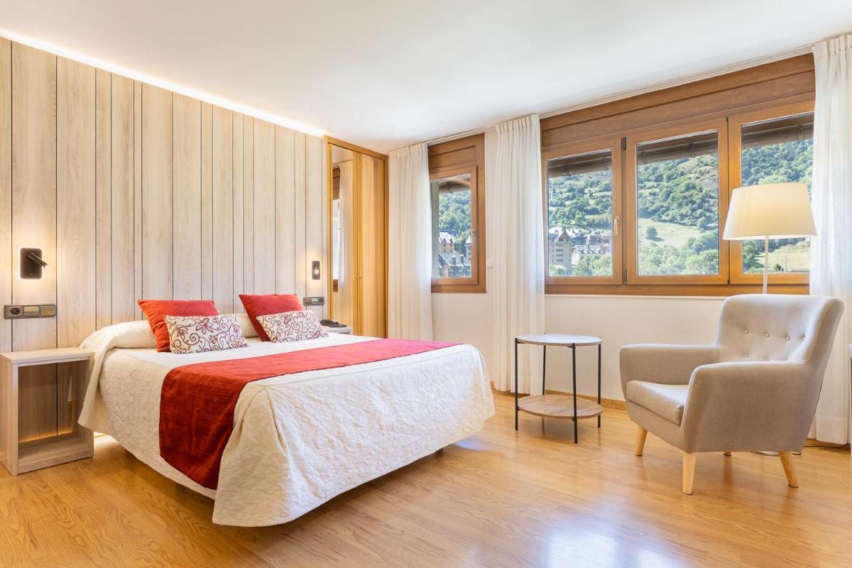 Un dormitorio con una cama y una silla y ventanas. en Hotel Eth Solan & SPA, en Vielha