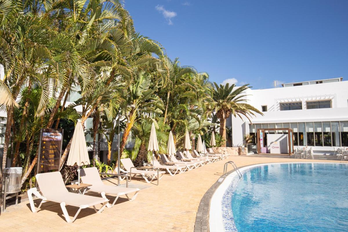 una piscina con sillas y sombrillas y palmeras en R2 Bahia Playa - Adults Only, en Tarajalejo