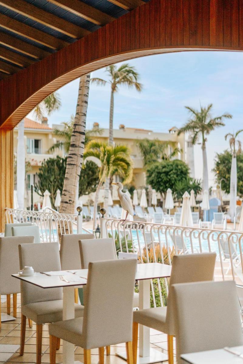 Un restaurante con mesas y sillas blancas y palmeras. en R2 Buganvilla Hotel & Spa, en Morro del Jable