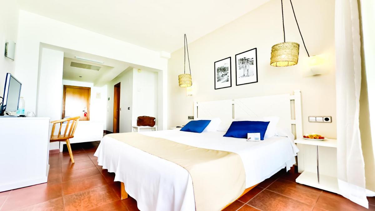 Un dormitorio blanco con una gran cama blanca con almohadas azules. en Hotel Na Forana, en Cala Ratjada