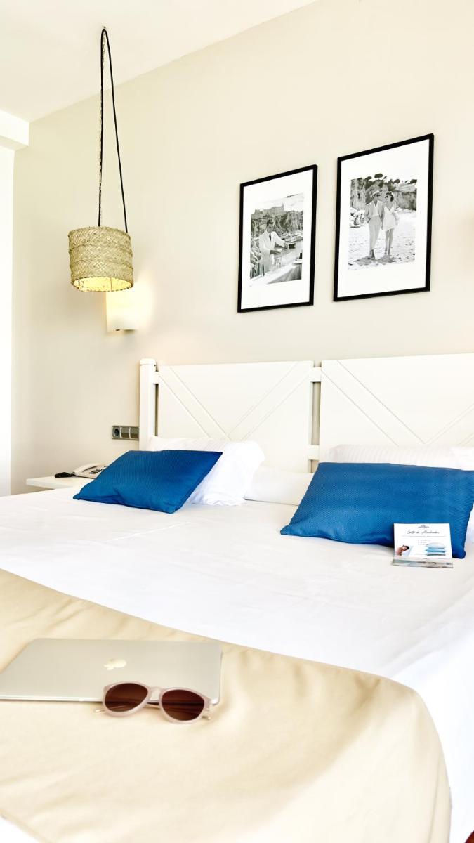 Una cama con almohadas azules y un par de gafas encima. en Hotel Na Forana, en Cala Ratjada