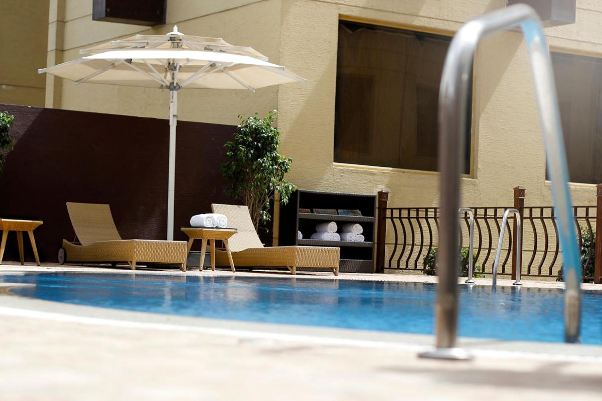 an outdoor swimming pool with chairs and an umbrella at Sterlings Mac Hotel in Bengaluru