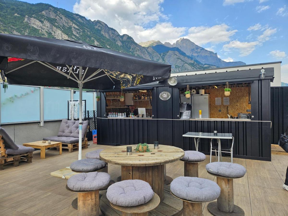 une terrasse avec des tables et des tabourets, avec des montagnes en arrière-plan dans l'établissement Best Western Coeur de Maurienne Hotel Restaurant & Spa, à Saint-Jean-de-Maurienne