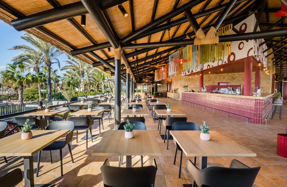 Un restaurante vacío con mesas y sillas de madera. en Barceló Fuerteventura Mar, en Caleta de Fuste